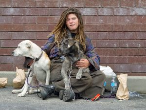 Homeless person cuddling dogs
