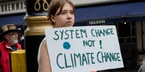 Extinction Rebellion protester holding a sign reading System Change Not Climate Change